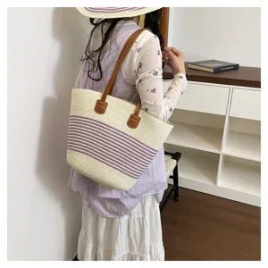 Detail view of a stylish straw woven tote bag featuring purple stripes and brown handles for summer beach.