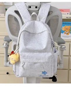 Detailed view of light grey nylon school backpack with front pocket and cute plush pendant.
