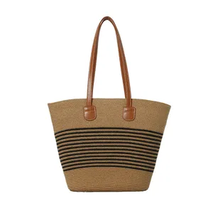 Detail view of the stylish woven straw tote bag with black stripes and brown handles.