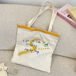 Detail view of canvas tote bag with artistic letter prints and yellow contrast trim.
