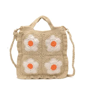 Dettaglio in primo piano della borsa in crochet beige con vivaci motivi floreali bianchi.