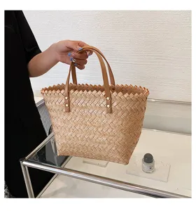 Woven straw handbag detail showing natural texture, brown leather handles and neat stitching.
