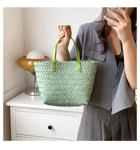Detailed view of a stylish green woven straw handbag with leather handles, casual summer daily use.