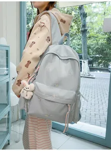 Vista detallada de la mochila bonita con bordado de lazos, bolsillo frontal y colgante de peluche.