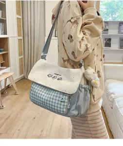 Bolso bandolera de cuadros azules y blancos con bordado de gato y detalles prácticos de estudiante.