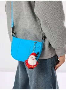 Detailansicht der blauen Umhängetasche mit Plüsch-Weihnachtsmann-Anhänger und Seitenetikett.