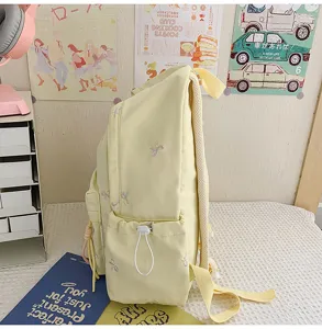 Detalle de mochila de estudiante amarillo claro con lindo bordado de lazo, bolso escolar amplio.