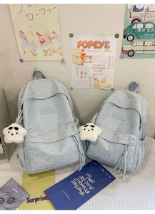 Détail de cartable scolaire bleu clair à motif d'étoiles mignon avec charm peluche et poche.