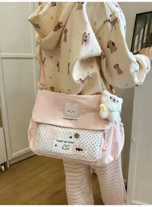 Cute pink canvas messenger bag for school girls with polka dot pocket and plush cat pendant.