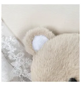 Dettaglio peluche orsetto beige morbido con orecchio di pelliccia e pizzo bianco grazioso.