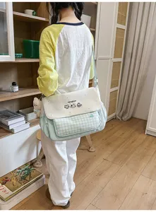Vista detallada del bolso bandolera de lona dulce con bolsillo de cuadros verdes y lindo estampado.
