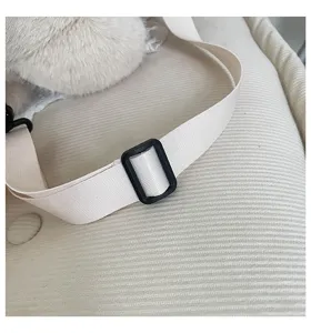 Dettaglio cinturino zaino orsetto peluche carino, tessuto beige morbido con fibbia.