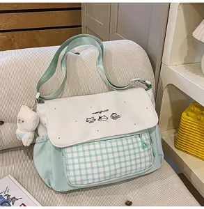 Primer plano de un bolso bandolera de cuadros verde menta y blanco con bordado de gato.