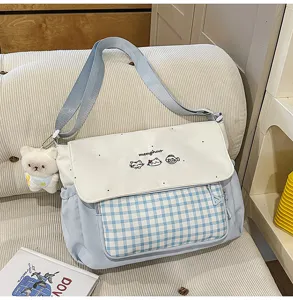 Detalle de bolso bandolera de lona a cuadros con bordado de gato y bolsillo frontal.