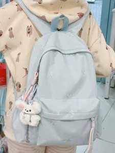 Mochila escolar azul claro con bordados de lazos de colores y colgante de oso de peluche.