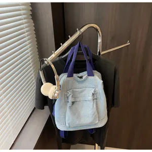 Detailed view of casual denim backpack with front pocket and blue straps hanging on display rack.