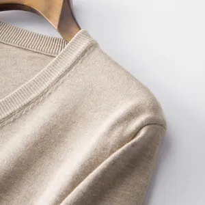 Close-up detail of beige V-neck knitted sweater shoulder and collar, fine knit texture.
