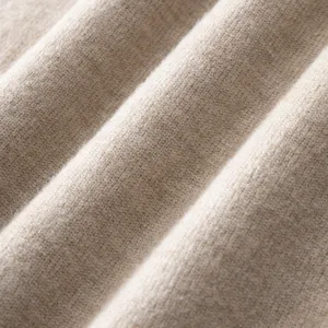 Knit sweater fabric close-up texture detail showing soft beige material and fine weave.