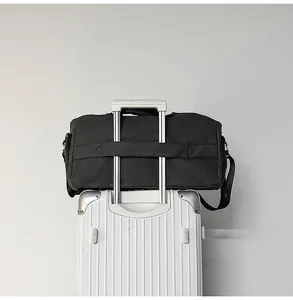 Detail view of black travel duffel bag with luggage sleeve on rolling suitcase in clean setting.
