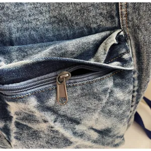 Denim backpack detail showcasing durable washed fabric, front zipper pocket, and fine stitching.