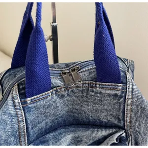 Denim backpack detail close-up, showing washed texture, blue webbed handles and double zippers.