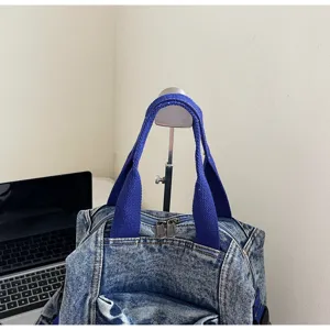 Close-up view of a washed denim backpack showcasing blue fabric handles and metal zippers.