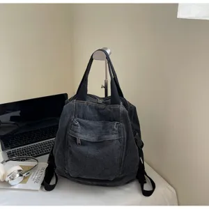 Detailed view of a dark grey washed denim backpack featuring front pocket and dual straps.