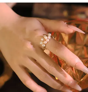 Hand close-up showing a delicate multi-pearl wire wrapped gold ring in warm cozy lighting.