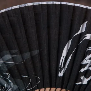 Detail close-up view of a black folding fan with elegant white brushstroke design and wooden ribs.