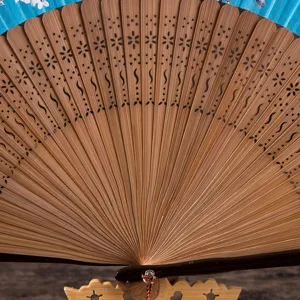 Close-up detail of traditional wooden folding hand fan ribs with delicate carved floral patterns.