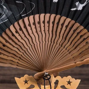 Close-up detail of traditional folding fan with carved bamboo ribs and black fabric pattern.