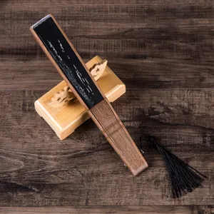 Wooden folding fan detail view with textured ribs, black tassel, and wooden stand.