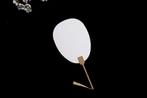 Gros plan détaillé d'éventail rond DIY en papier blanc avec une poignée en bambou fin.