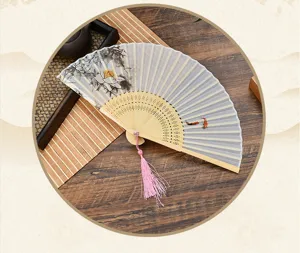 Chinese style folding fan with delicate lotus pattern and pink tassel, elegant bamboo design.