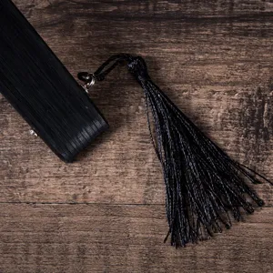 Detailed view of a black folding fan handle with elegant tassel on wood background.