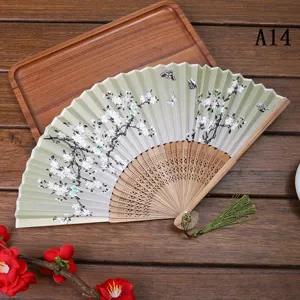 Vue détaillée d'un éventail pliant chinois en tissu dégradé vert, fleurs et pompon.