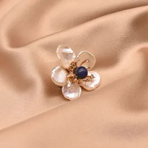 Detail shot of baroque pearl flower brooch featuring deep blue center stone and delicate gold metal.
