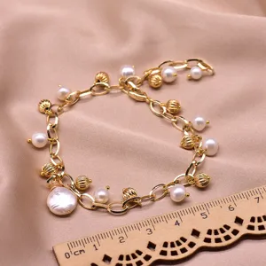 Close-up detail of gold pearl charm bracelet with freshwater pearls and fluted beads on fabric.