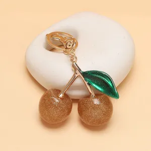 Nahaufnahme Detail des glänzenden goldenen Glitzer-Kirsch-Taschenanhängers mit grünem Blatt.