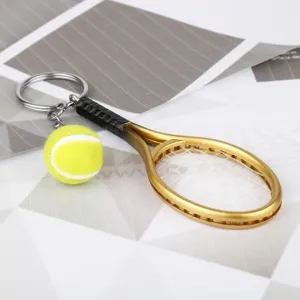 Portachiavi in miniatura racchetta da tennis dorata con pallina, elegante accessorio sportivo in metallo.