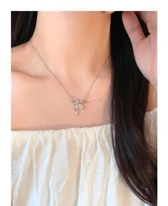 Primer plano detallado de un delicado collar con colgante de lazo de plata con circonitas brillantes.