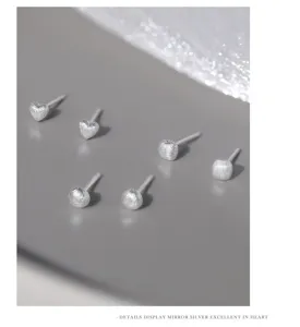Primeros planos de detalles de pendientes de tuerca geometricos de plata pura esmerilada.