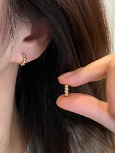 Close-up detail view of minimalist gold-plated beaded small hoop earrings worn on ear.