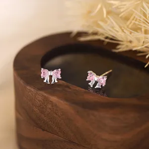 Gros plan de boucles d'oreilles nœud en cristal rose sur un support en bois foncé.