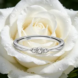 Primer plano detallado del anillo de plata S925 con tres piedras sobre rosa con rocío.