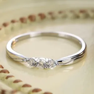 Detalle de anillo de plata con tres piedras brillantes, diseño minimalista fino.