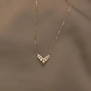 Vista detallada del collar con colgante de perlas y diamantes en forma de V, cadena de plata elegante.