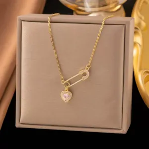 Close-up of gold safety pin necklace with pink heart cubic zirconia pendant in jewelry box.