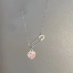 Detail view of silver safety pin pink heart crystal pendant, delicate clavicle chain jewelry.