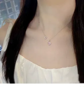 Close-up detail of silver safety pin necklace featuring sparkling pink heart zircon pendant.